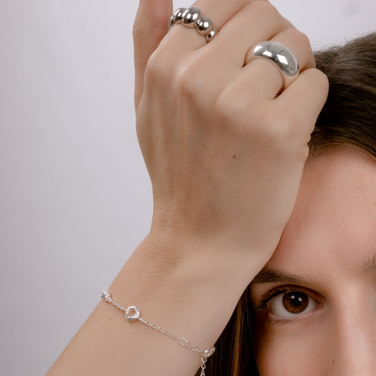 Close-up of a person wearing silver rings and a bracelet on a plain background